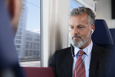 Mature businessman sitting train, using earphones - FKF03583