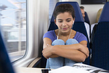 Teenage girl traveling alone by train, listening music, reading a book - FKF03591