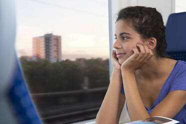 Jugendliches Mädchen reist allein mit dem Zug und schaut aus dem Fenster - FKF03594