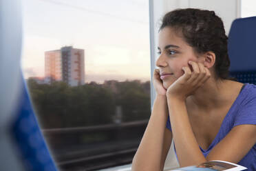 Teenage girl traveling alone by train, looking out of window - FKF03594