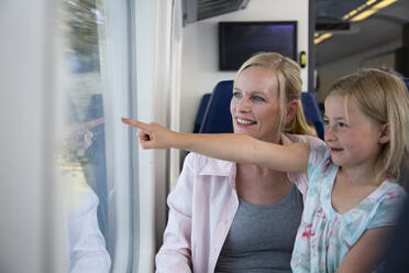 Mother and daughter traveling by train, pointing out of window - FKF03609