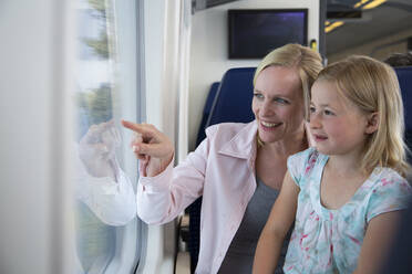 Mother and daughter traveling by train, pointing out of window - FKF03610