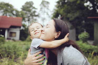 Affectionate mother hugging toddler in garden - KMKF01034