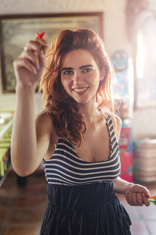 Porträt einer glücklichen jungen Frau, die in einer Sportbar Darts spielt, lizenzfreies Stockfoto