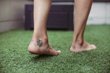 Close-up of a woman's tattooed foot walking on artificial grass - ACPF00609