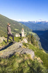 Frau blickt auf alte Kirche in den Bergen, Alp San Romerio, Brusio, Kanton Graubünden, Poschiavo-Tal, Schweiz, Europa - RHPLF04690
