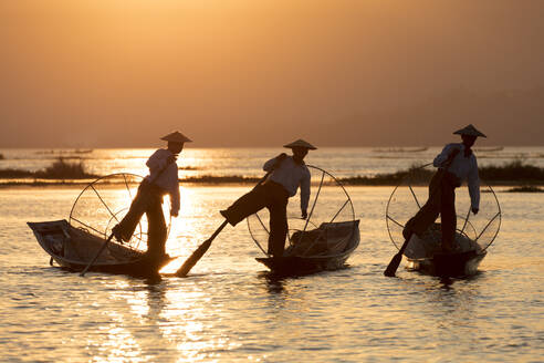 Drei Fischer rudern mit einem Bein bei Sonnenuntergang auf dem Inle-See, Shan-Staat, Myanmar (Birma), Asien - RHPLF04910