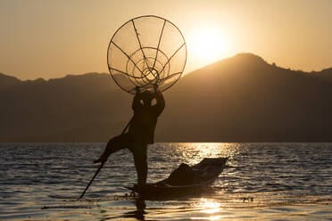 Ein Fischer steht auf einem Bein und hält sein Fischernetz bei Sonnenuntergang am Inle-See, Shan-Staat, Myanmar (Birma), Asien - RHPLF04912