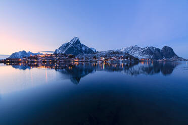 Überblick über das Dorf und die schneebedeckten Gipfel in der Abenddämmerung, Reine Bay, Lofoten-Inseln, Nordland, Norwegen, Europa - RHPLF05008