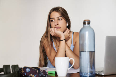 Studentin, die zu Hause lernt und traurig zur Seite schaut, lizenzfreies Stockfoto