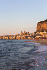 Blick vom Strand entlang der Wasserkante auf die Stadt und die zum UNESCO-Weltkulturerbe gehörende arabisch-normannische Kathedrale, Sonnenuntergang, Cefalu, Palermo, Sizilien, Italien, Mittelmeer, Europa - RHPLF05907