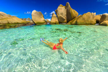 Glückliche Frau im Bikini liegt im türkisfarbenen Wasser im natürlichen Pool am Strand der Seychellen, Anse Marron, La Digue, Seychellen, Indischer Ozean, Afrika - RHPLF06205