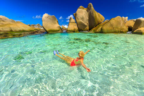 Glückliche Frau im Bikini liegt im türkisfarbenen Wasser im natürlichen Pool am Strand der Seychellen, Anse Marron, La Digue, Seychellen, Indischer Ozean, Afrika - RHPLF06205