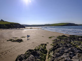 Ein Surfer geht an einem sonnigen Morgen in Bigbury-on-Sea, Devon, England, Vereinigtes Königreich, Europa, zu seiner Session - RHPLF06603