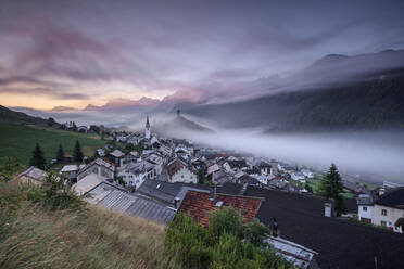 Rosa Wolken und Nebel über dem Dorf Ardez in der Morgendämmerung, Bezirk Inn, Unterengadin, Kanton Graubünden, Schweiz, Europa - RHPLF06816