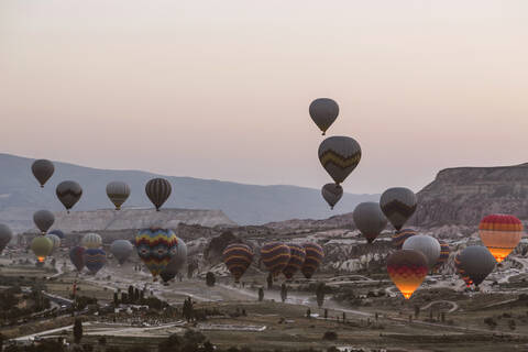 Bunte Heißluftballons fliegen über die Landschaft gegen den klaren Himmel im Goreme National Park, Kappadokien, Türkei, lizenzfreies Stockfoto