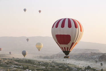 Bunte Heißluftballons fliegen über Land gegen den klaren Himmel im Goreme National Park, Türkei - KNTF03278