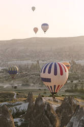 Bunte Heißluftballons fliegen bei Sonnenuntergang über das Land im Goreme-Nationalpark, Kappadokien, Türkei - KNTF03279