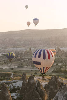 Bunte Heißluftballons fliegen bei Sonnenuntergang über das Land im Goreme-Nationalpark, Kappadokien, Türkei - KNTF03279