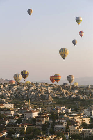 Bunte Heißluftballons fliegen über Gebäude gegen den klaren Himmel im Goreme National Park, Kappadokien, Türkei, lizenzfreies Stockfoto