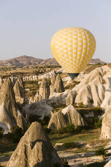 Gelber Heißluftballon fliegt über Land gegen den klaren Himmel im Goreme Nationalpark, Kappadokien, Türkei - KNTF03283