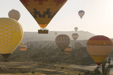 Mehrfarbige Heißluftballons fliegen bei Sonnenuntergang über die Berge im Goreme-Nationalpark, Kappadokien, Türkei - KNTF03286