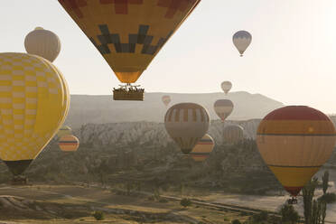 Multi colored hot air balloons flying over mountains at Goreme National Park during sunset, Cappadocia, Turkey - KNTF03286