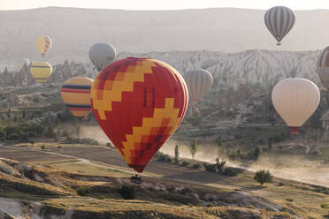 Mehrfarbige Heißluftballons fliegen bei Sonnenuntergang über das Land im Goreme-Nationalpark, Kappadokien, Türkei - KNTF03287