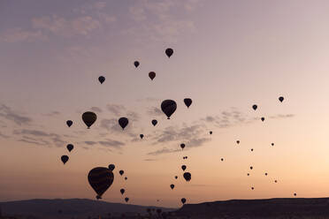 Silhouette Heißluftballons fliegen über Berge gegen Himmel in der Türkei bei Sonnenuntergang, Kappadokien - KNTF03288