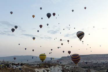 Bunte Heißluftballons fliegen über Landschaft gegen Himmel in der Türkei während des Sonnenuntergangs, Kappadokien - KNTF03289