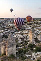 Bunte Heißluftballons fliegen über felsige Landschaft gegen den Himmel bei Sonnenuntergang in Kappadokien, Türkei - KNTF03290