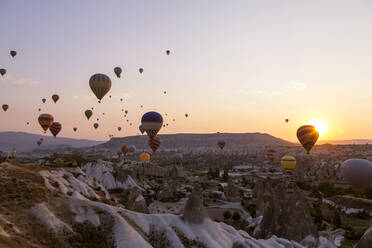 Bunte Heißluftballons fliegen über felsige Landschaft bei Sonnenuntergang in Goreme, Kappadokien, Türkei - KNTF03291