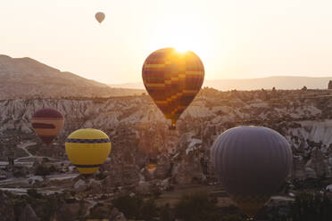 Bunte Heißluftballons fliegen über die felsige Landschaft in Goreme bei Sonnenuntergang, Kappadokien, Türkei - KNTF03292