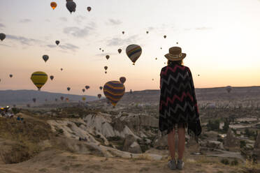 Young woman and hot air balloons in the evening, Goreme, Cappadocia, Turkey - KNTF03297