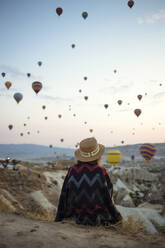 Young woman and hot air balloons in the evening, Goreme, Cappadocia, Turkey - KNTF03298