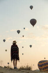 Young woman and hot air balloons in the evening, Goreme, Cappadocia, Turkey - KNTF03300