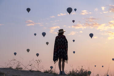 Young woman and hot air balloons in the evening, Goreme, Cappadocia, Turkey - KNTF03301