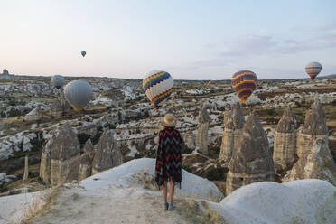 Young woman and hot air balloons in the evening, Goreme, Cappadocia, Turkey - KNTF03302