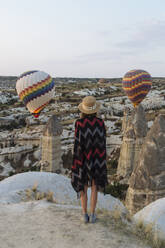 Young woman and hot air balloons in the evening, Goreme, Cappadocia, Turkey - KNTF03303