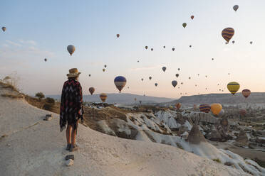 Young woman and hot air balloons in the evening, Goreme, Cappadocia, Turkey - KNTF03304