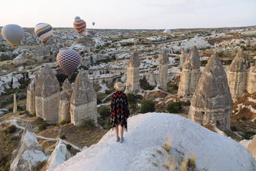 Young woman and hot air balloons in the evening, Goreme, Cappadocia, Turkey - KNTF03305