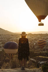 Young woman and hot air balloons in the evening, Goreme, Cappadocia, Turkey - KNTF03306