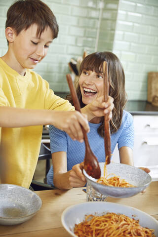 Mutter isst Spaghetti mit ihrem Sohn in der Küche, lizenzfreies Stockfoto