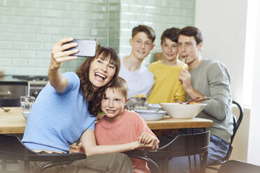 Mother and her four sons taking smartphone selfies at lunch - MCF00171