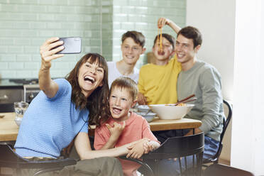 Mother and her four sons taking smartphone selfies at lunch - MCF00173