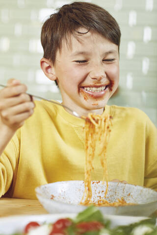 Unordentlicher Junge isst Spaghetti mit Tomatensoße, lizenzfreies Stockfoto