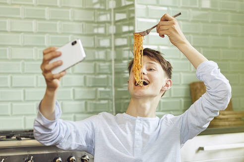 Laughing boy taking smartphone selfie, eating spaghetti - MCF00183