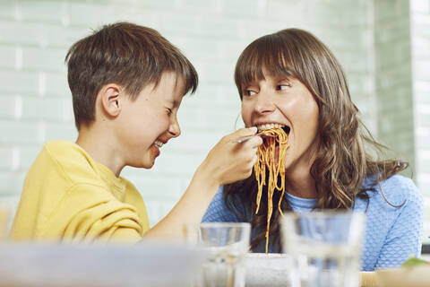 Sohn füttert Mutter mit Spaghetti in der Küche, lizenzfreies Stockfoto