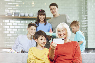 Mother and sons celebrating grandmother's bithday in their kitchen, boy taking selfies - MCF00213