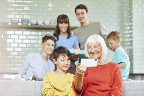 Mutter und Söhne feiern den Geburtstag ihrer Großmutter in ihrer Küche, der Junge macht Selfies - MCF00213